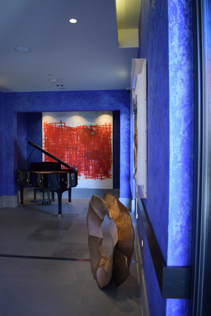 Bout du couloir en enduit bleu avec piano et toile rouge au mur