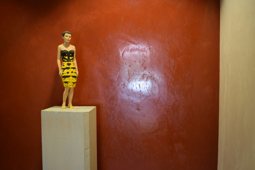 Mur enduit rouge avec statuette femme en jaune devant